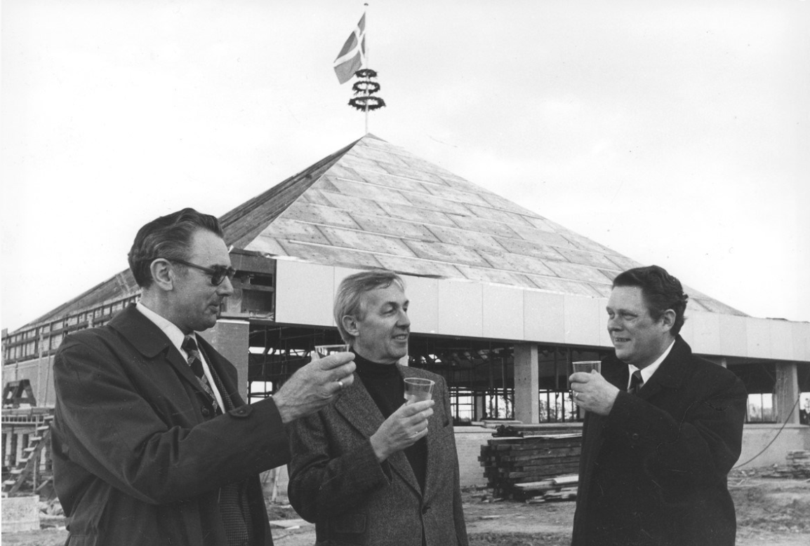 Rejsegildet i oktober 1977 af den første version af Hollænderhallens Svømmehal med den genkendelige pyramide  over ”den dybe ende” af idrætsbassinet. Fra venstre daværende  borgmester Albert Svendsen, arkitekt Paul Grønning og svømmeklubbens mangeårige formand Tage Welander. (Arkiv.dk)